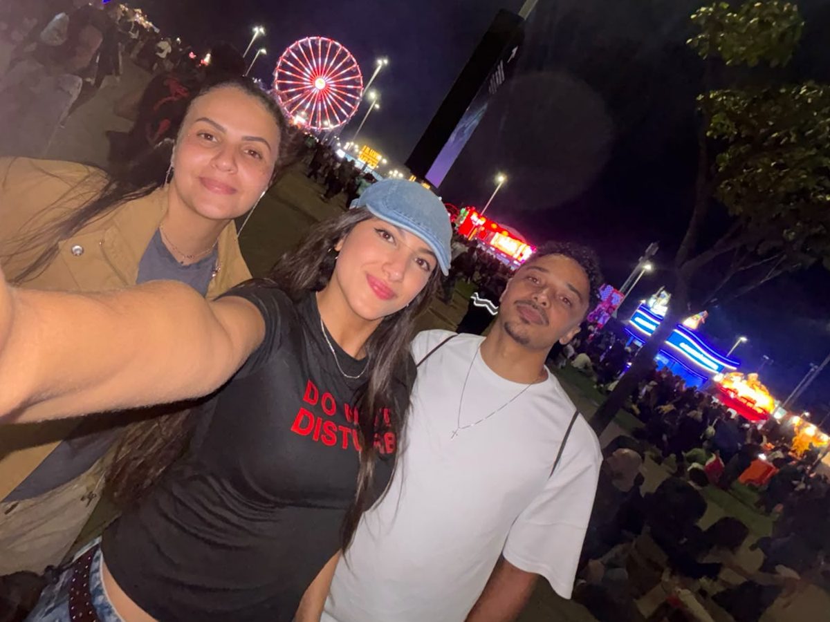 Nicole com os primos Mariana Paixão e Sávio Oliveira em um festival à noite, com uma roda-gigante iluminada ao fundo